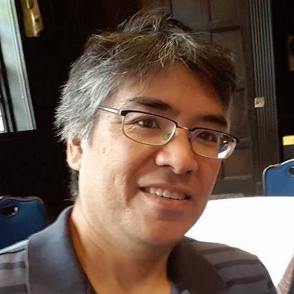 This is a headshot of an Asian American male with short black hair and wearing eyeglasses and a blue-striped knit shirt.