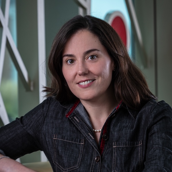 This is a headshot of a women with shoulder-length dark hair and wearing a dark denim shirt dress and pearls.