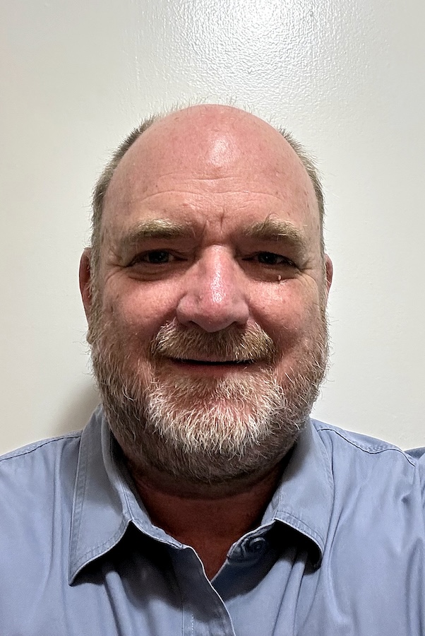 Headshot of a man in front of a white background wearing a light blue button-down shirt.